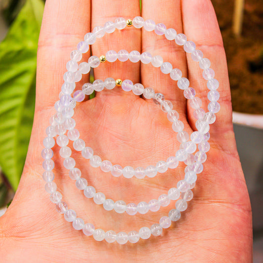 Hand holding multiple 4mm Aquamarine bracelets with gold-filled accent beads, showing translucency and natural blue glow.