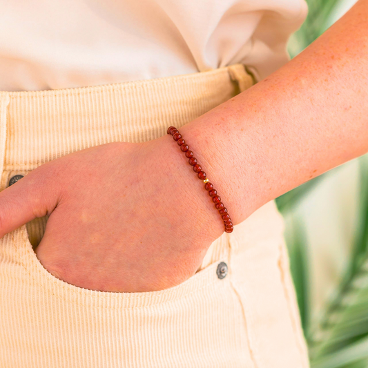 A minimal red carnelian bead bracelet with a 14k gold-filled accent bead shown on a person’s wrist for size reference.