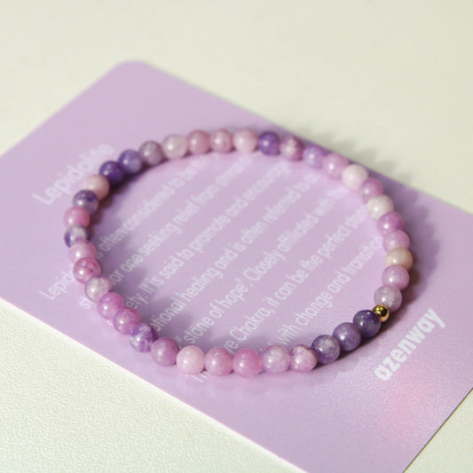 Close-up photo of the Lepidolite bracelet resting on its purple Azenway meaning card, showing the soft pink and purple gemstone beads with a gold-filled accent.