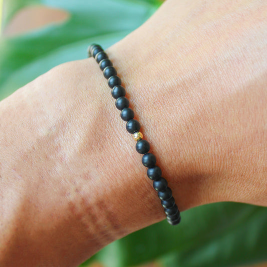 Matte black onyx bracelet with one gold-filled bead shown worn on a wrist for size and fit reference.