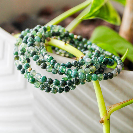 Stack of Moss Agate gemstone bracelets with green natural patterns and gold-filled beads displayed on a plant stem.