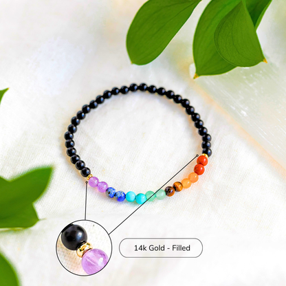 7 Chakra gemstone bracelet placed on white fabric with leaves, featuring a highlighted 14k gold-filled accent bead.