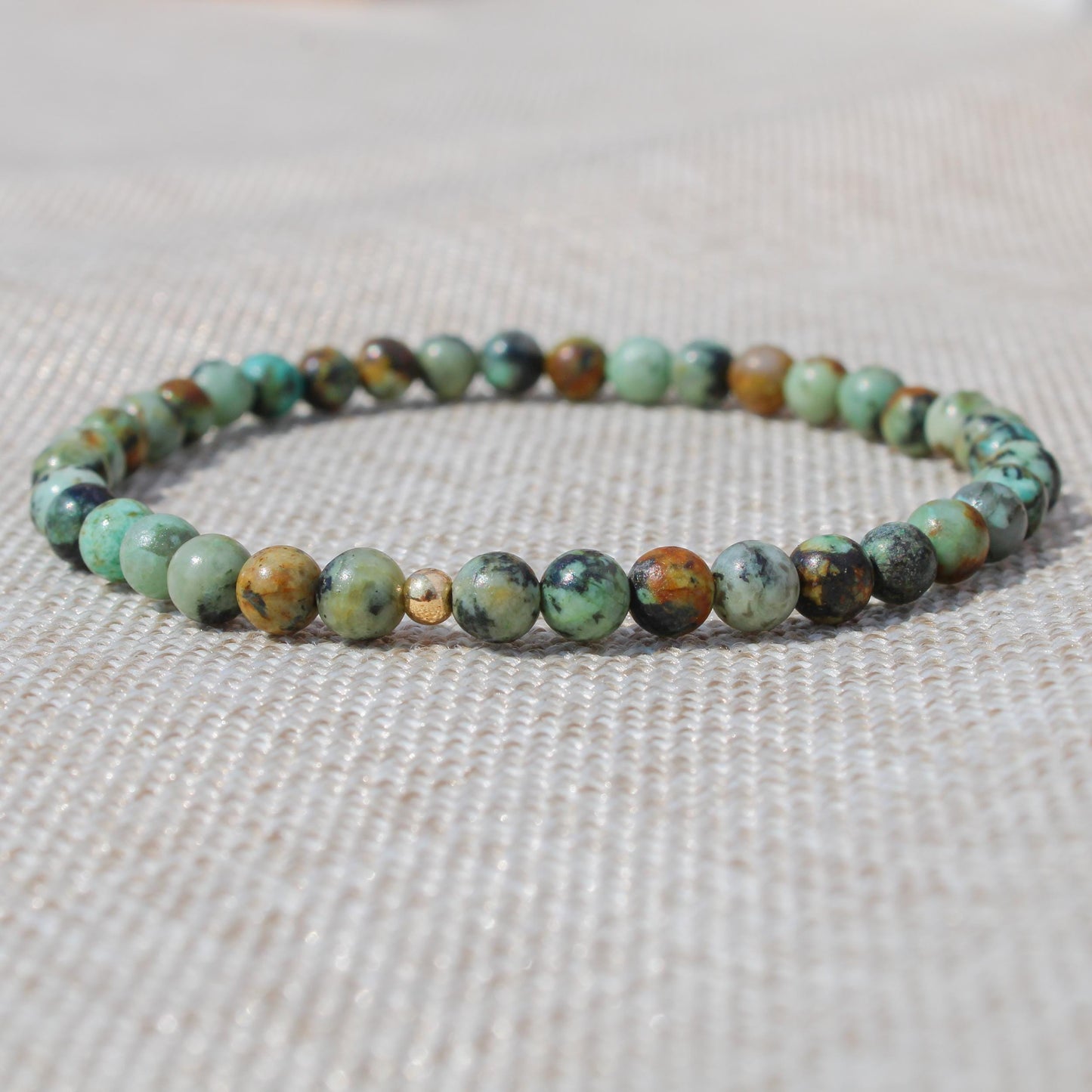 Close-up of an African Turquoise beaded bracelet with a 14k gold-filled accent bead on neutral fabric.
