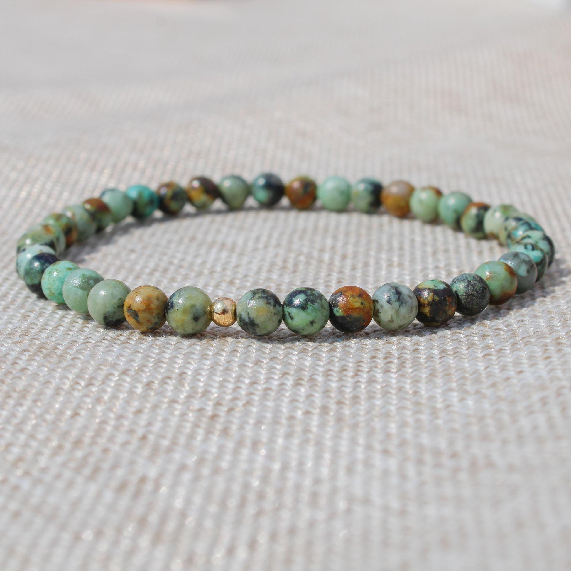 Close-up of an African Turquoise beaded bracelet with a 14k gold-filled accent bead on neutral fabric.