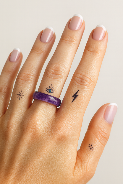 Woman’s hand wearing an Amethyst crystal ring with minimalist spiritual tattoos and French tip nails