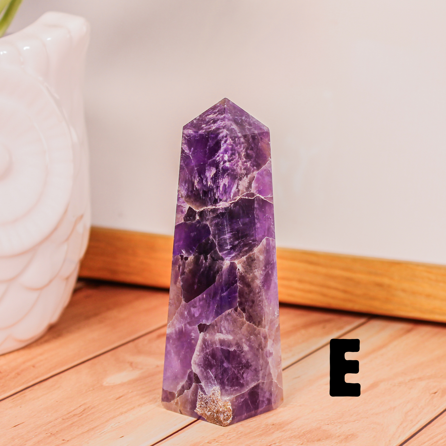 Amethyst crystal tower labeled E polished purple stone point photographed on wooden surface