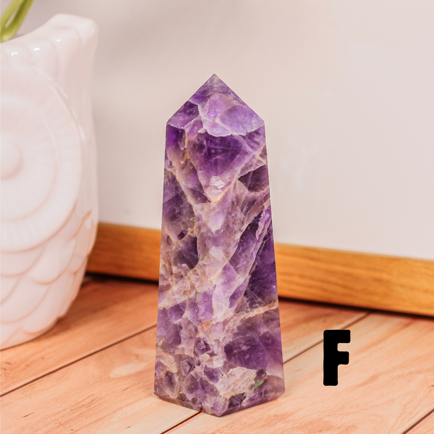 Amethyst crystal tower labeled F polished purple stone point photographed on wooden surface