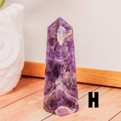 Amethyst crystal tower labeled H polished purple stone point photographed on wooden surface