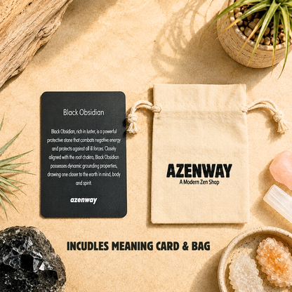 Black Obsidian crystal meaning card displayed beside an Azenway organic cotton drawstring gift bag with "Includes Meaning Card & Bag" text overlay. Set on a warm neutral background with Black Obsidian crystal accents and botanical décor, showcasing the premium packaging included with every Black Obsidian purchase.
