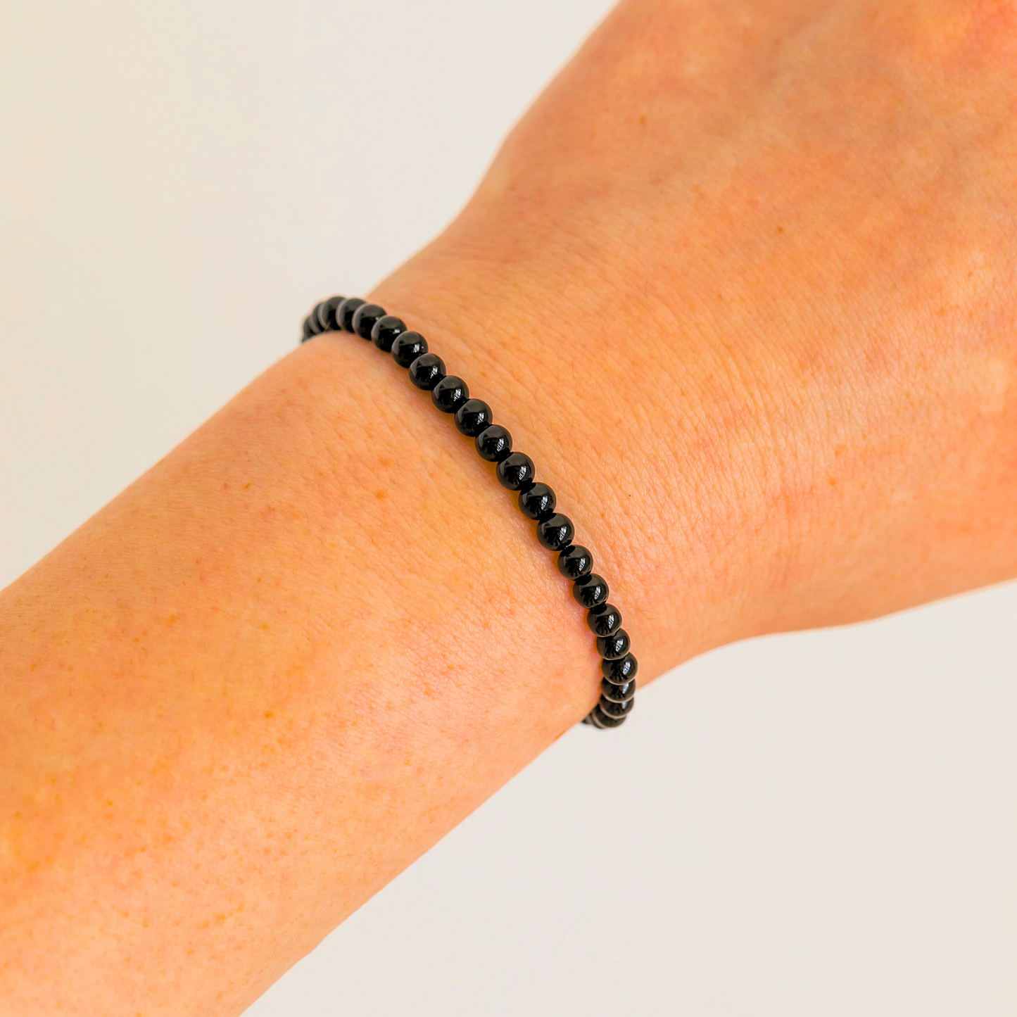 Black Tourmaline 4mm beaded bracelet worn on wrist, minimalist crystal jewelry.
