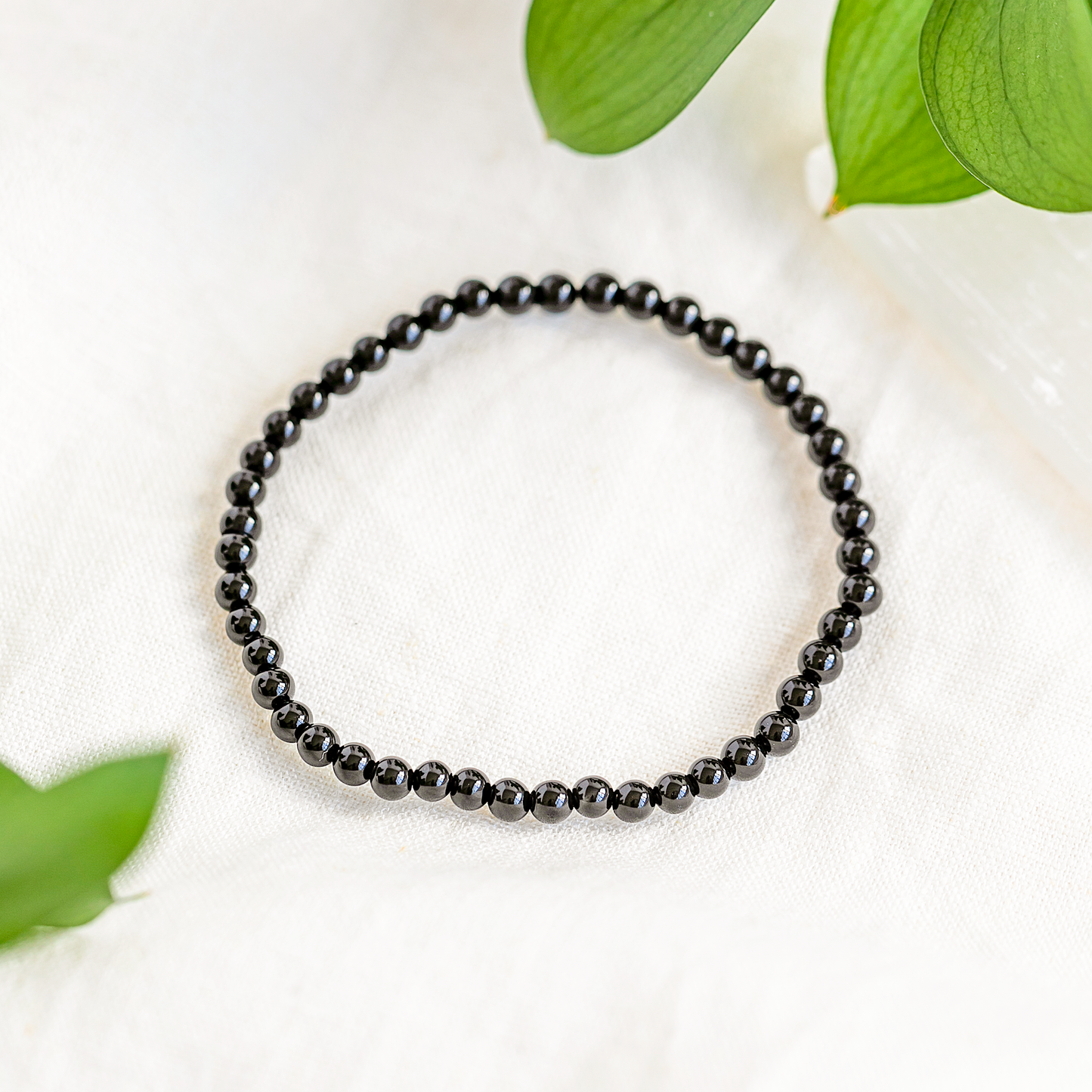 Black Tourmaline 4mm beaded bracelet displayed on a white cloth with soft green leaves.