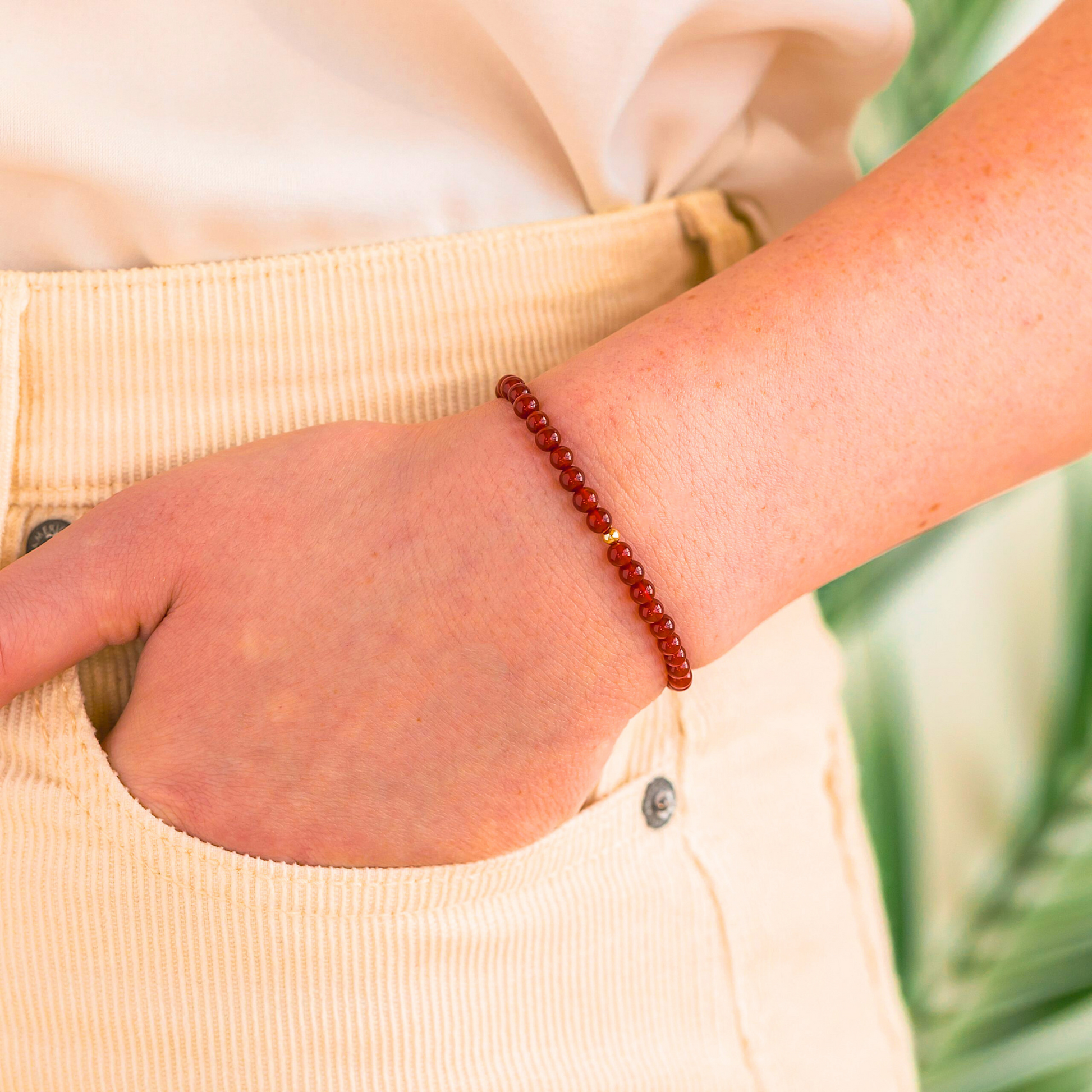 A minimal red carnelian bead bracelet with a 14k gold-filled accent bead shown on a person’s wrist for size reference.
