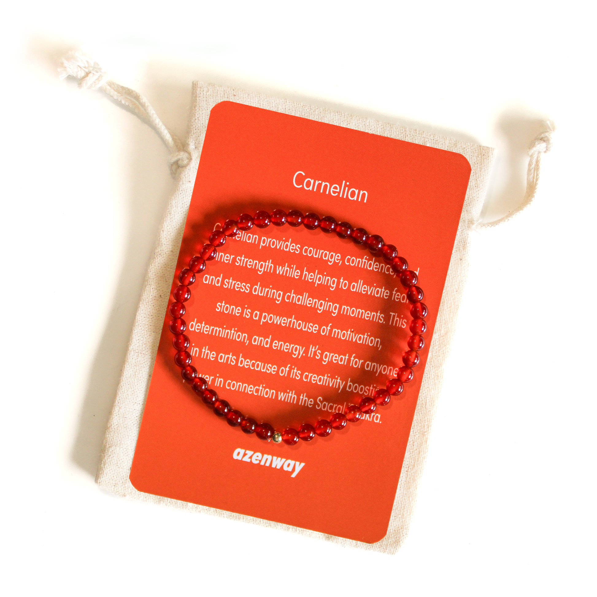 A red carnelian gemstone bracelet displayed on top of a matching orange Azenway meaning card and cotton bracelet bag.