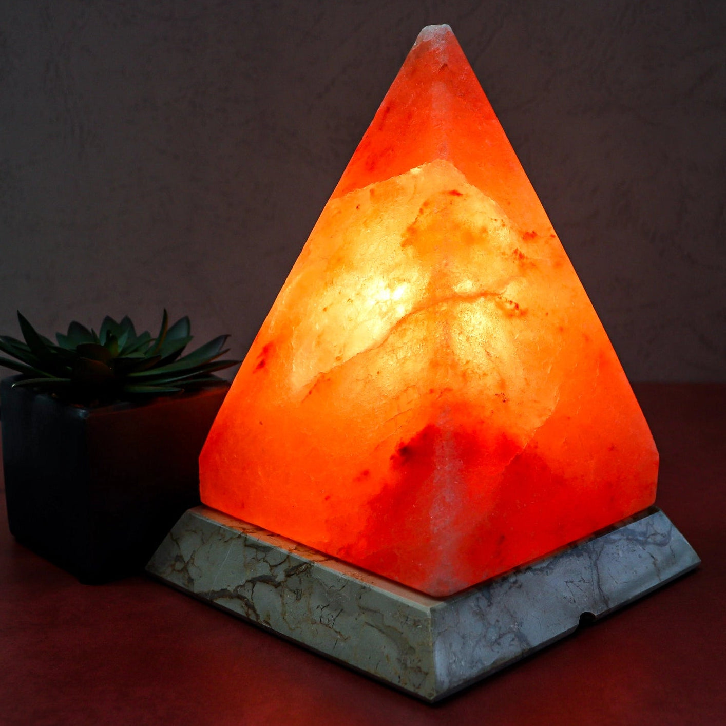 Triangular Himalayan salt lamp on a dark surface with a plant in the background
