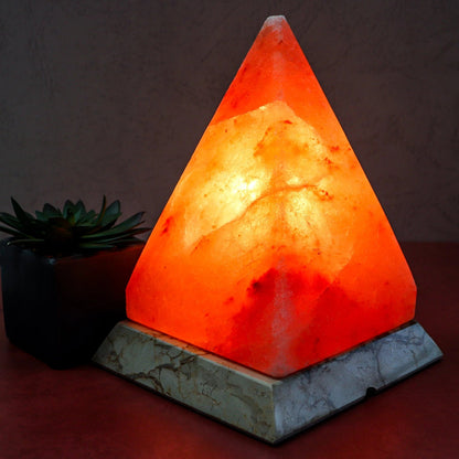 Triangular Himalayan salt lamp on a dark surface with a plant in the background