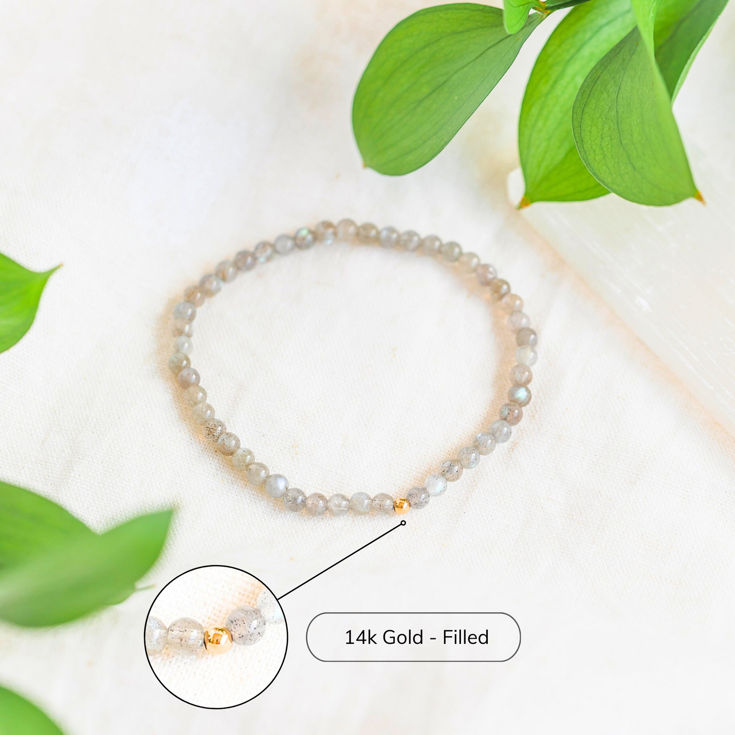 Azenway labradorite bracelet in a bright flat lay with greenery, highlighting the grey flash of the stones and the single gold-filled bead.