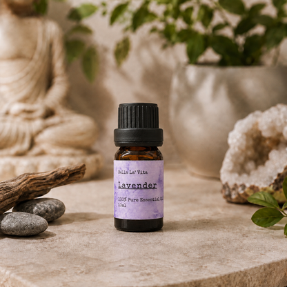 Amber 10 ml bottle of Bella La' Vita Lavender 100% Pure Essential Oil displayed on a warm zen-inspired stone surface with a Buddha statue, driftwood, smooth stones, greenery, and a crystal geode in the background.