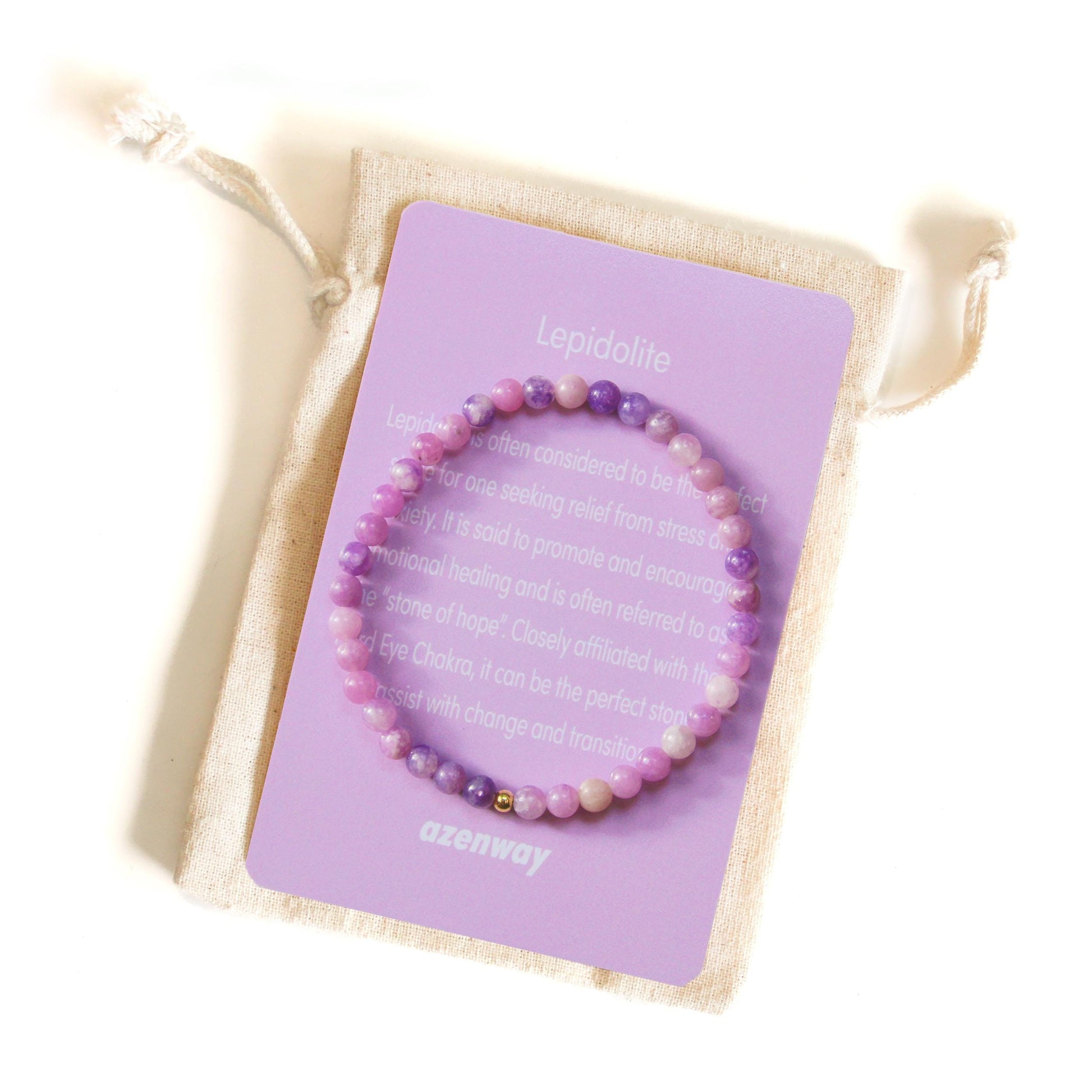 Lepidolite crystal bracelet with gold-filled accent displayed on its lavender Azenway meaning card and organic cotton pouch.