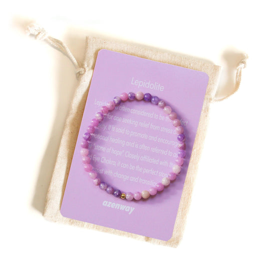 Lepidolite crystal bracelet with gold-filled accent displayed on its lavender Azenway meaning card and organic cotton pouch.