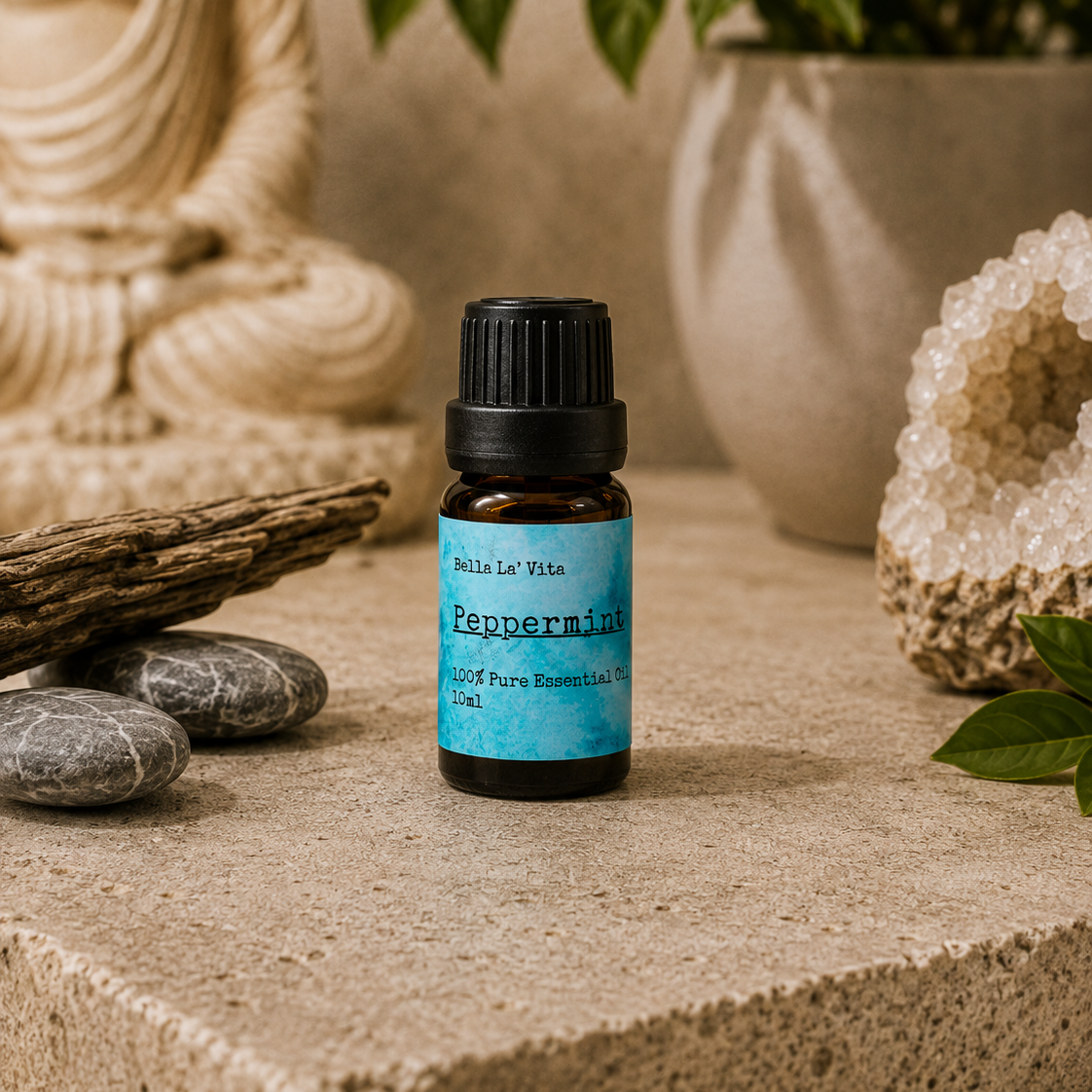 Amber 10 ml bottle of Bella La' Vita Peppermint 100% Pure Essential Oil displayed on a warm zen-inspired stone surface with a Buddha statue, driftwood, smooth stones, greenery, and a crystal geode in the background.