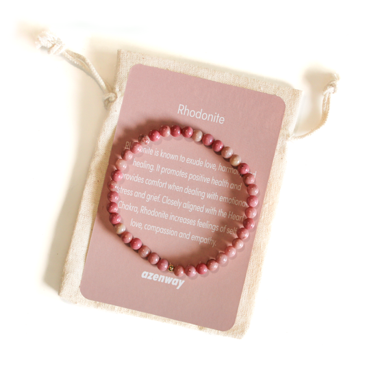 Rhodonite crystal bracelet displayed on an Azenway meaning card and cotton gift bag, showing its soft pink tones and gold accent bead.