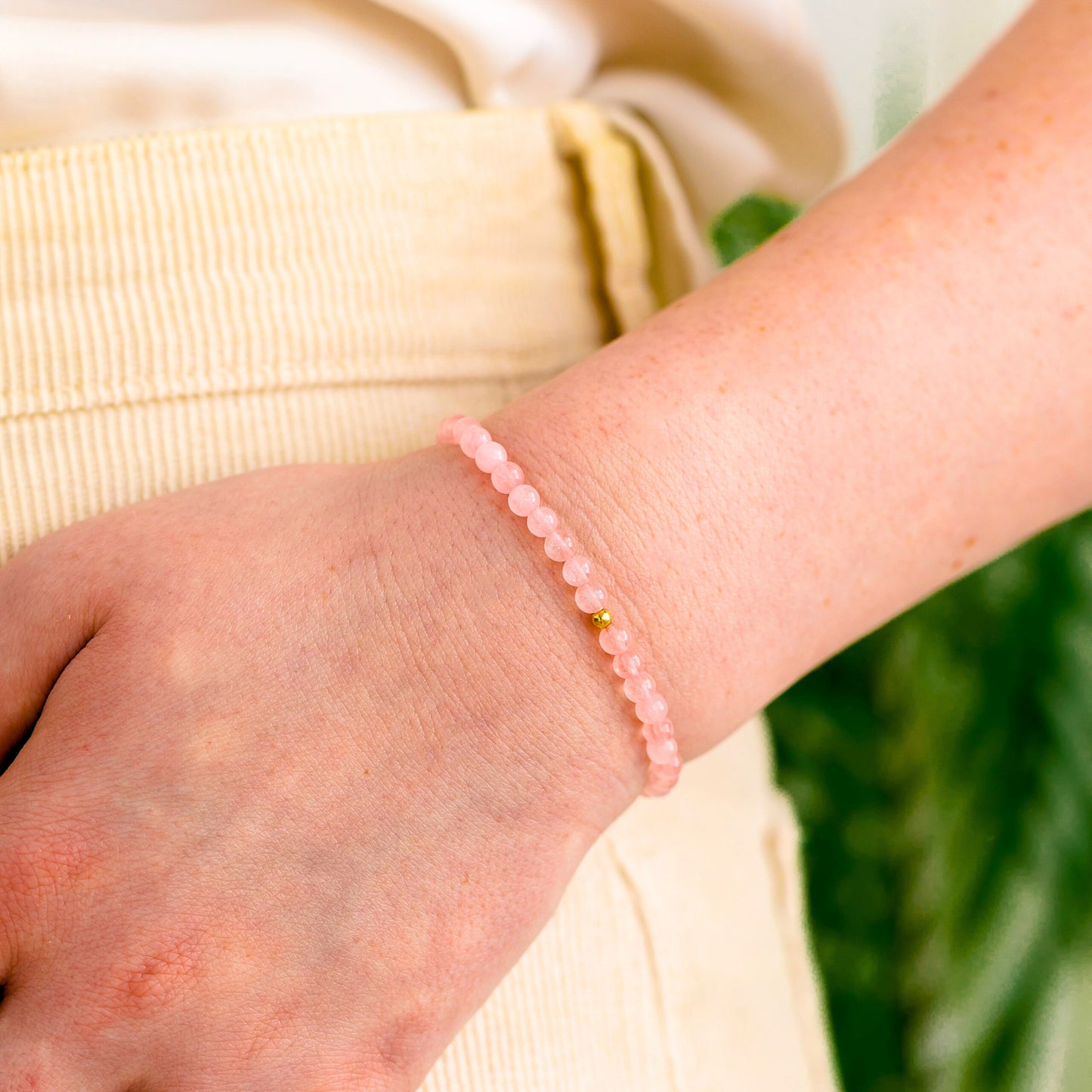 Close-up of a Rose Quartz bracelet with one gold-filled bead worn on a wrist, showing the soft pink gemstone beads.