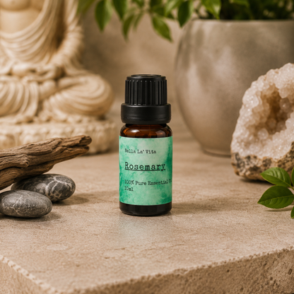 Amber 10 ml bottle of Bella La' Vita Rosemary 100% Pure Essential Oil displayed on a warm zen-inspired stone surface with a Buddha statue, driftwood, smooth stones, greenery, and a crystal geode in the background.