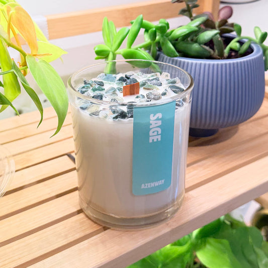 Sage scented crystal candle topped with green stones and wooden wick on a wooden plant shelf