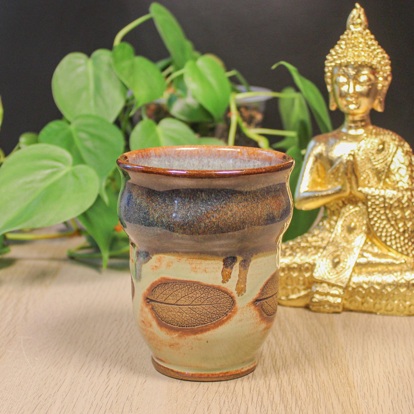 Handmade ceramic sage leaf cup by Emma Stewart, earthy glazed pottery cup with leaf imprint, styled with plant and Buddha decor