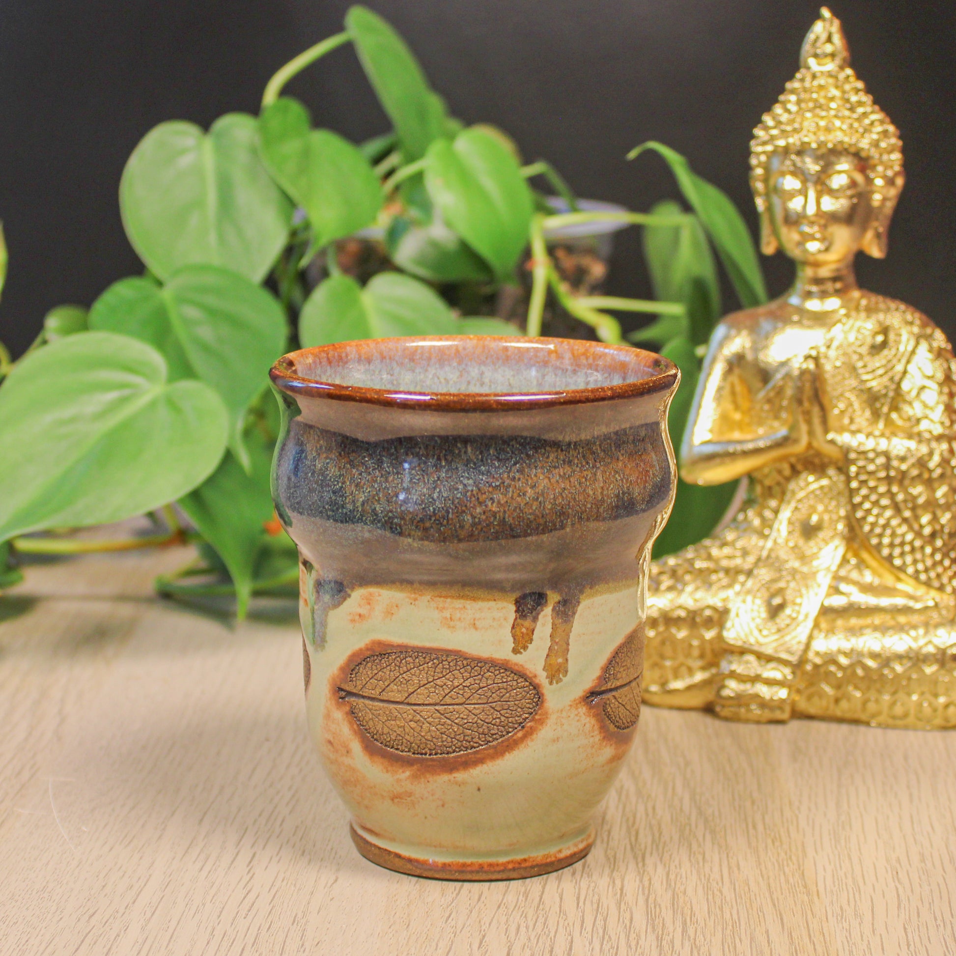 Handmade ceramic sage leaf cup by Emma Stewart, earthy glazed pottery cup with leaf imprint, styled with plant and Buddha decor