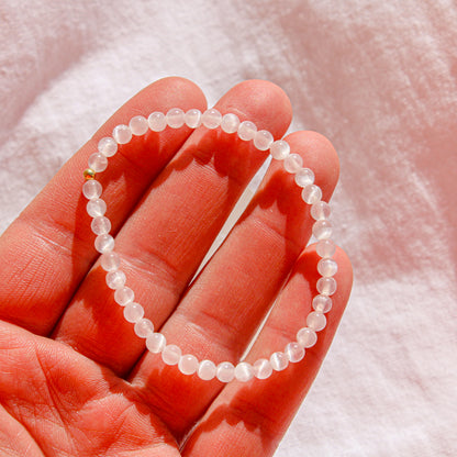 Close-up of a 4mm Selenite crystal bracelet with a single gold-filled bead shown in natural light in the palm of a hand.