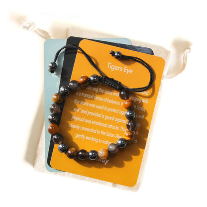 Azenway Triple Protection Bracelet displayed on its Tiger’s Eye meaning card, featuring Tiger’s Eye, Black Obsidian and Hematite beads with an adjustable black cord.