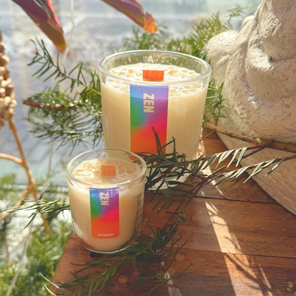 Large and small Zen aromatherapy candles with wooden wicks displayed in sunlight surrounded by greenery at Azenway.