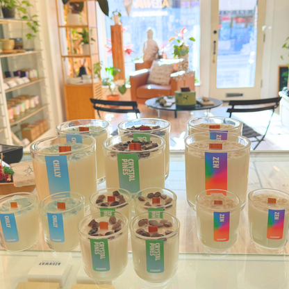 Azenway shop display showing Zen and Crystal Pines candles with wooden wicks arranged on a glass counter with plants in the background.