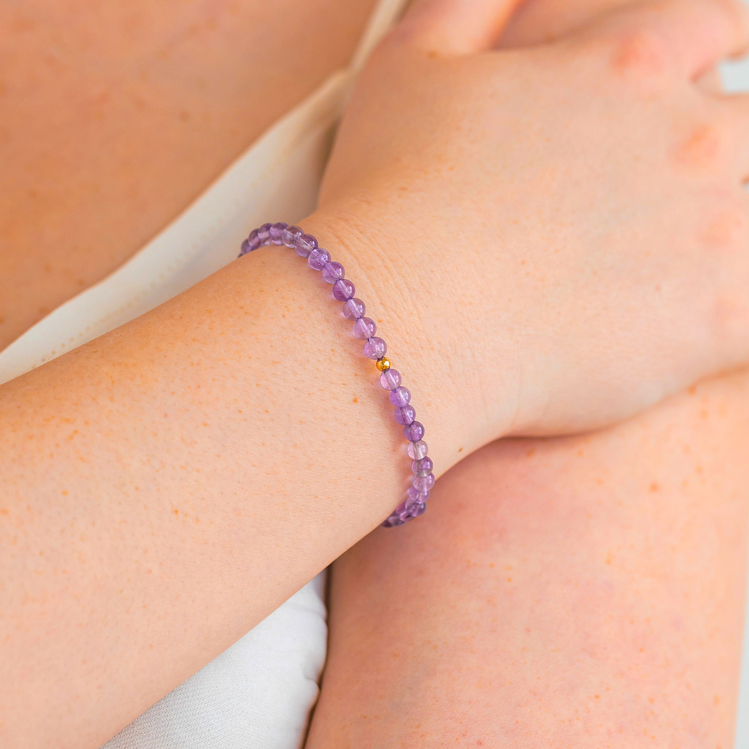 Amethyst gemstone bracelet with gold-filled bead shown on wrist in a soft lifestyle setting.