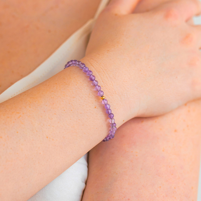 Amethyst gemstone bracelet with gold-filled bead shown on wrist in a soft lifestyle setting.