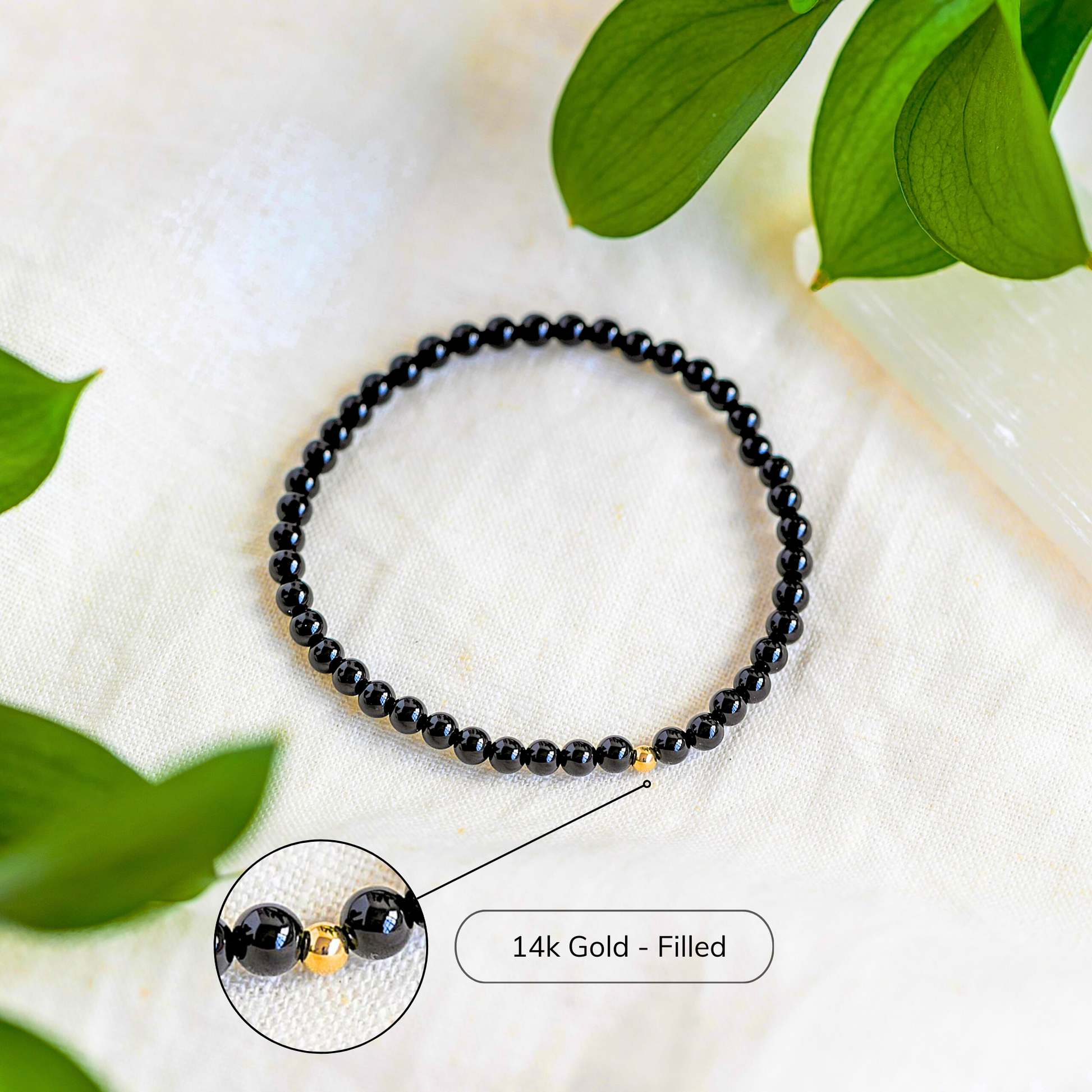 Black Tourmaline gemstone bracelet with gold-filled bead styled among greenery on a neutral surface.