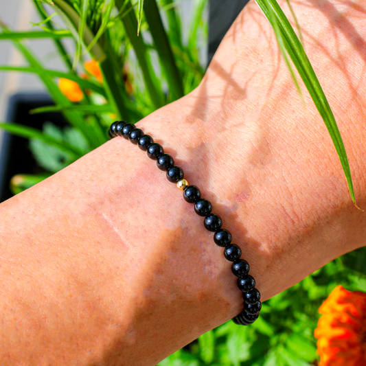 Black Tourmaline gemstone bracelet with gold-filled accent shown on wrist in natural outdoor light.