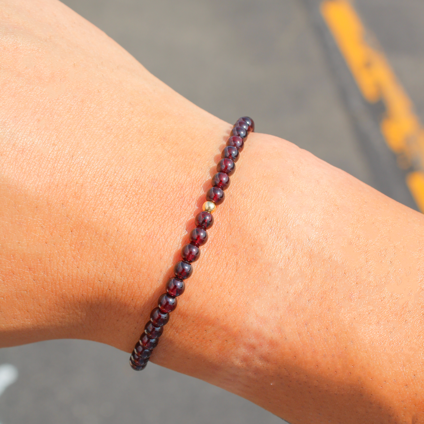 Garnet gemstone bracelet with gold-filled bead shown on wrist in natural sunlight.
