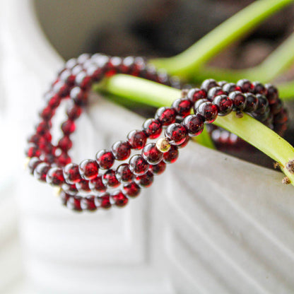 Stack of Garnet gemstone bracelets with gold-filled accents styled on plant stem.