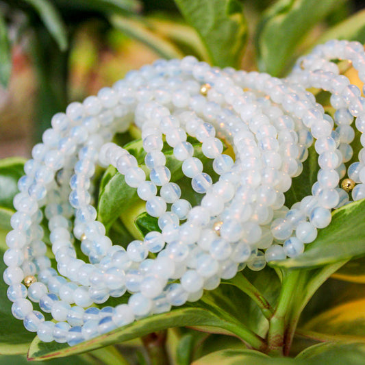 Multiple Opalite gemstone bracelets with gold-filled accents styled among leafy greenery.