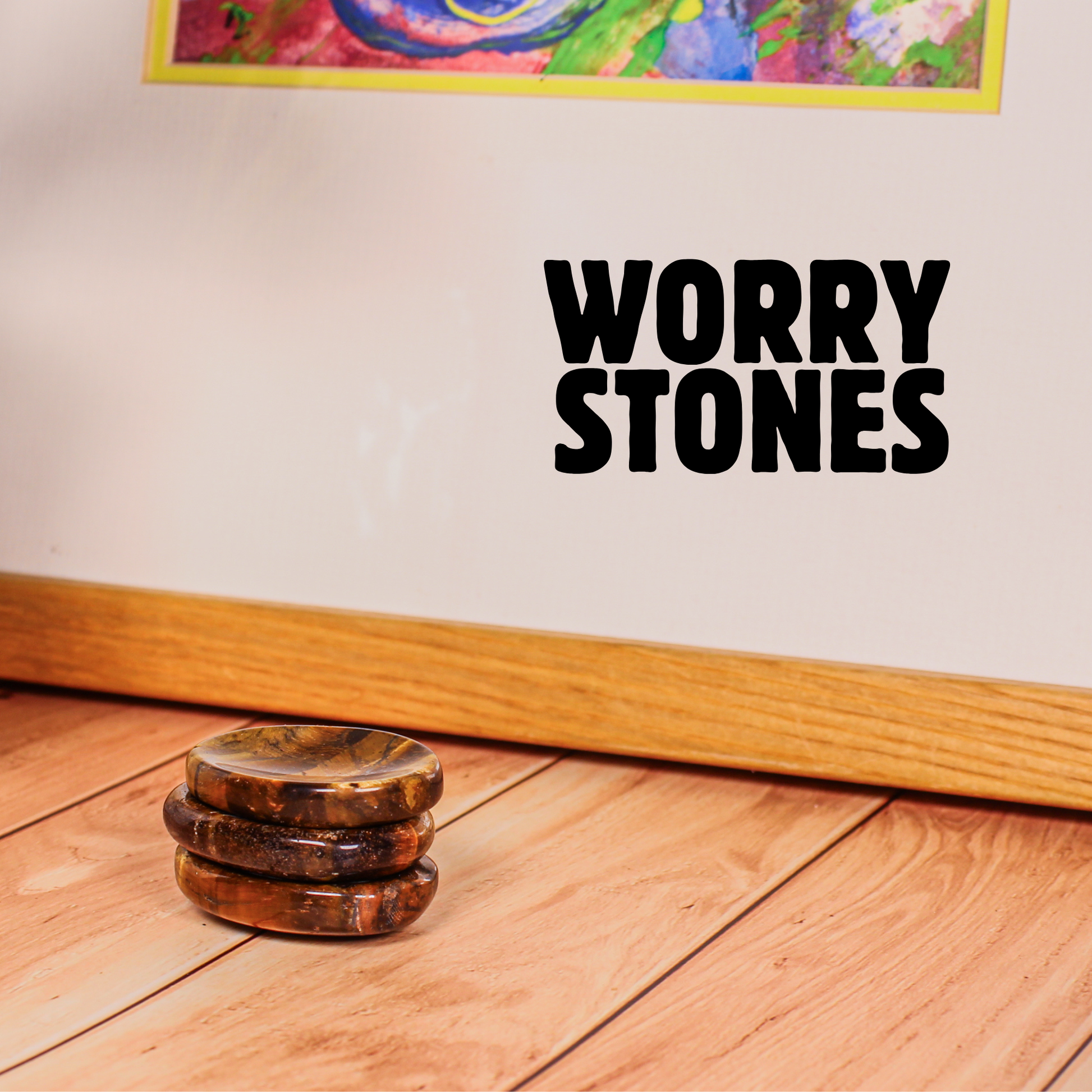 Stack of tiger’s eye crystal worry stones on wooden floor with “Worry Stones” text above